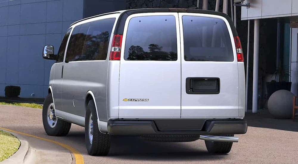 A silver 2021 Chevy Express passenger van is shown from the rear in front of an office building.