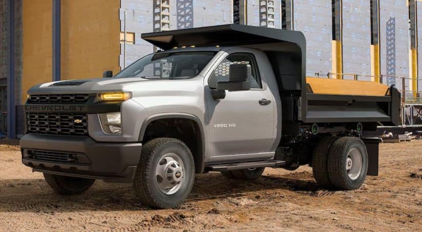 A silver 2021 Chevy Silverado 3500 HD Chassis Cab dump truck is parked at a job site.