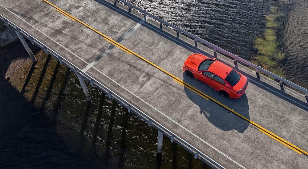 An orange 2021 Dodge Charger Scat Pack Widebody is shown from a high angle driving over a bridge.