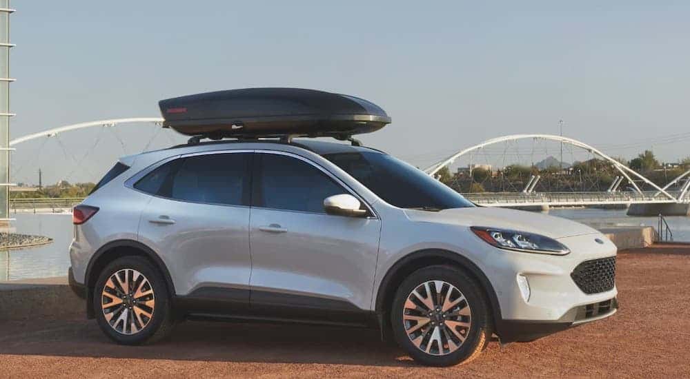 A white 2021 Ford Escape with cargo on the roof is parked in front of a river and bridge.