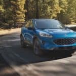 A blue 2021 Ford Escape is driving on a winding forest road after winning the 2021 Ford Escape vs 2021 Mazda CX-5 comparison.