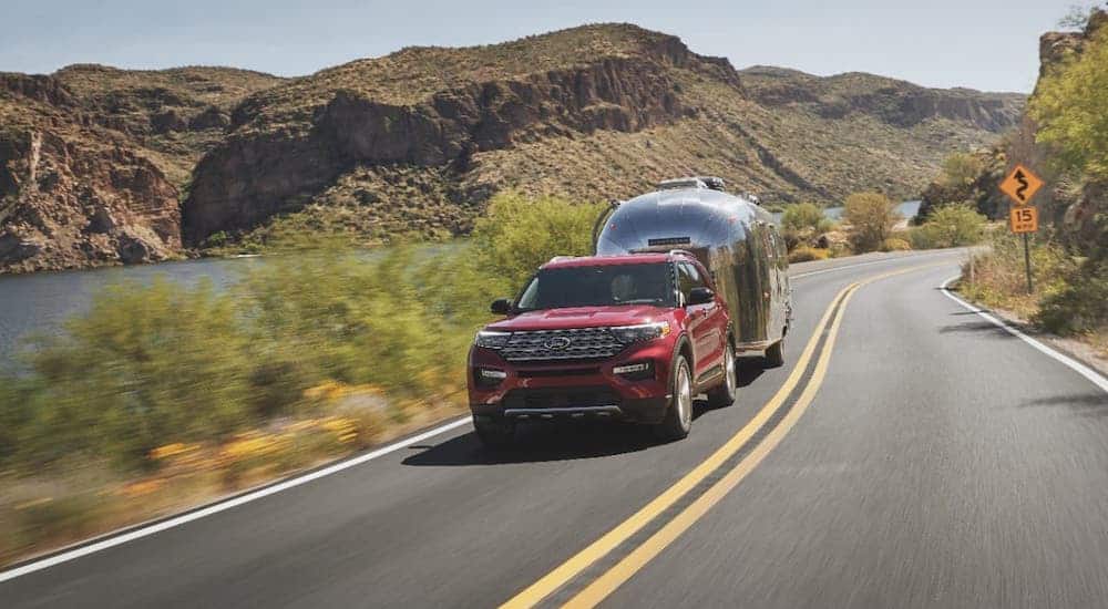 A red 2021 Ford Explorer is towing an Airstream camper on an empty highway.