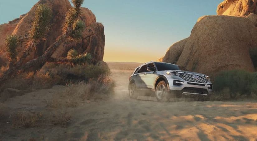 A silver 2021 Ford Explorer is driving between two rock formations in a desert.