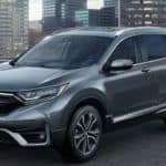 A popular 2021 Honda Hybrid, a grey 2021 Honda CR-V Hybrid, is parked in an empty lot with a cityscape in the background.