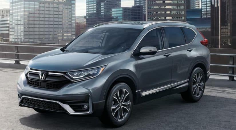 A popular 2021 Honda Hybrid, a grey 2021 Honda CR-V Hybrid, is parked in an empty lot with a cityscape in the background.