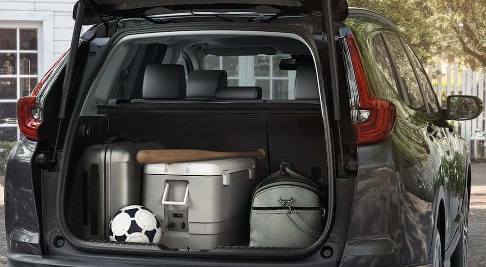 A dark grey 2021 Honda CR-V Hybrid is shown from behind with luggage and sports gear in the trunk.