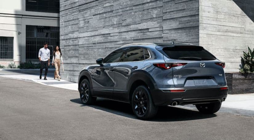 A blue 2021 Mazda CX-30 is shown from the rear parked in front of a modern stone building with a couple approaching it.