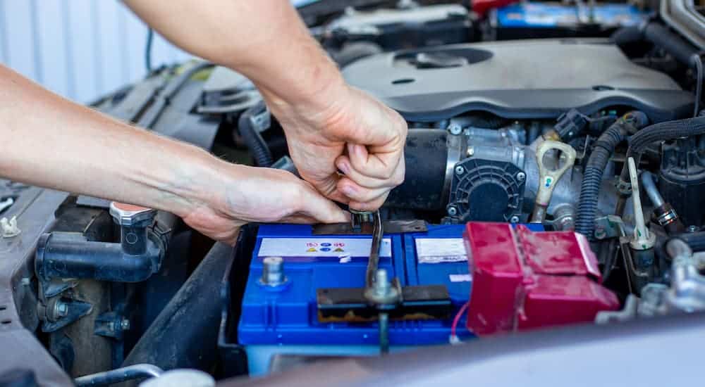 A close up is shown of a person replacing the battery on a car, which is common car maintenance item on most vehicles.