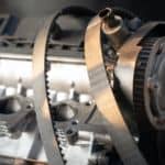 A close up is shown on an engine with accessory belts draped over the top.