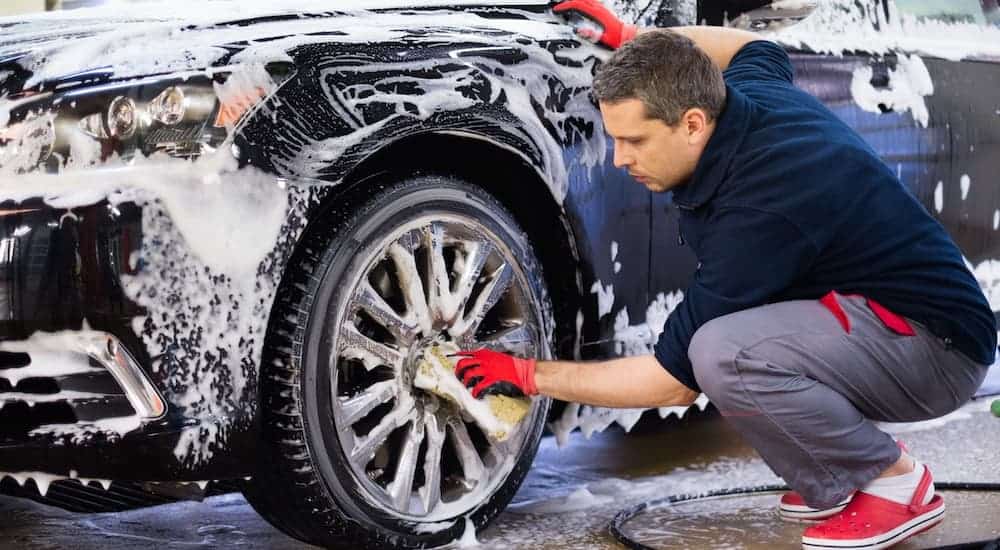 A close up is shown of a man washing the wheel of a car.