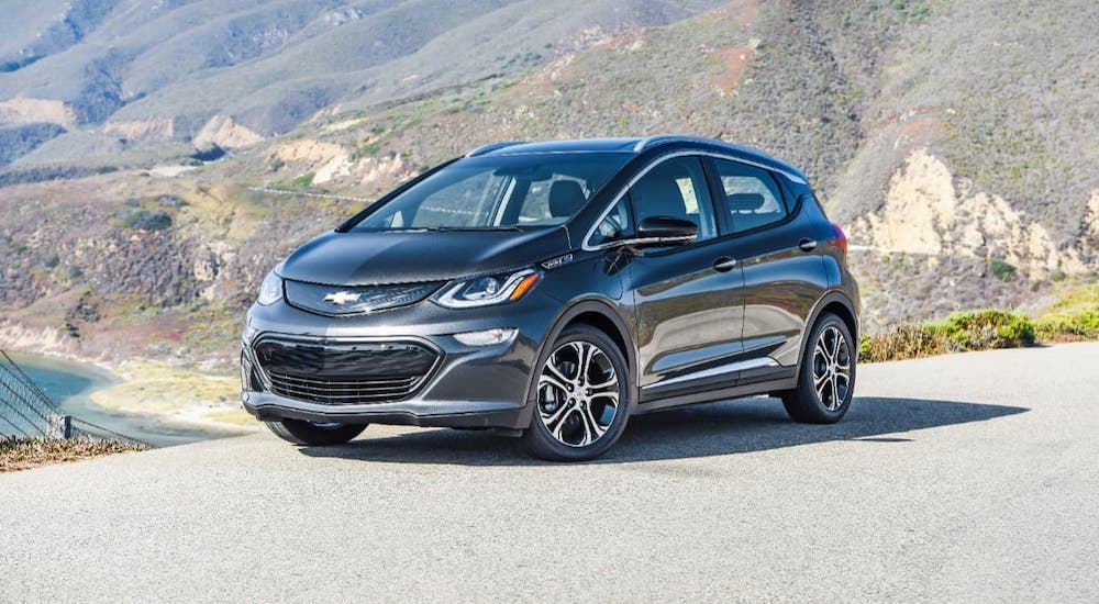A black 2021 Chevy Bolt EV is parked on a hill overlooking mountains and a bay.