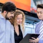 A salesman is showing a couple information on a clipboard.