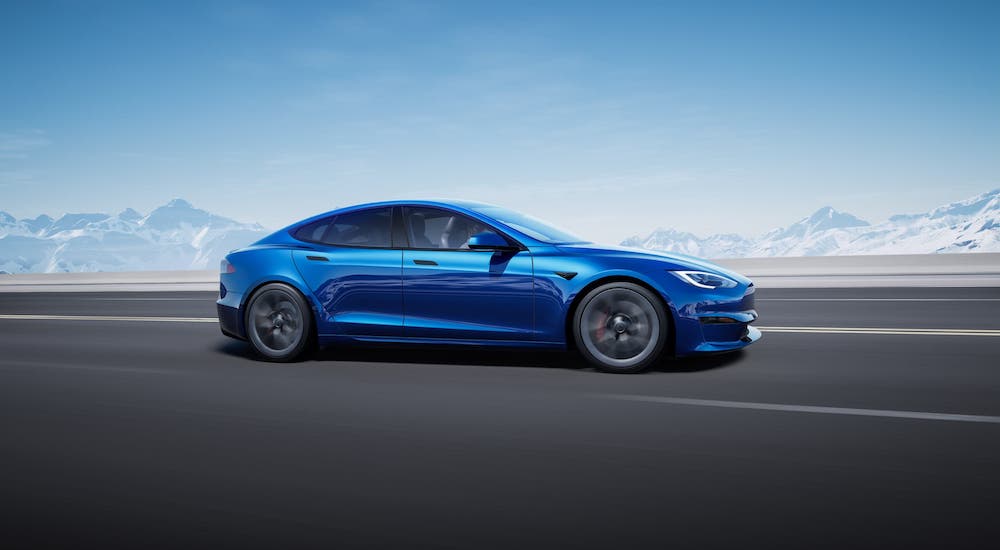 A trendsetter among electric vehicles, a blue 2021 Tesla Model S, is shown from the side driving on an empty highway.