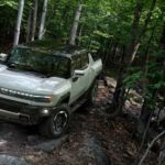 A white 2022 GMC Hummer EV is shown driving through the woods.