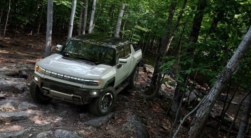 A white 2022 GMC Hummer EV is shown driving through the woods.