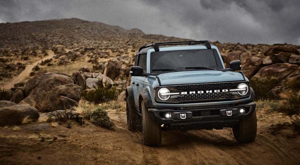 A blue 2021 Ford Bronco 4-door from a local Ford dealer is climbing over rocks.