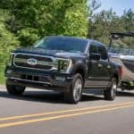 A black 2021 Ford F-150 Limited is towing a boat on a highway.