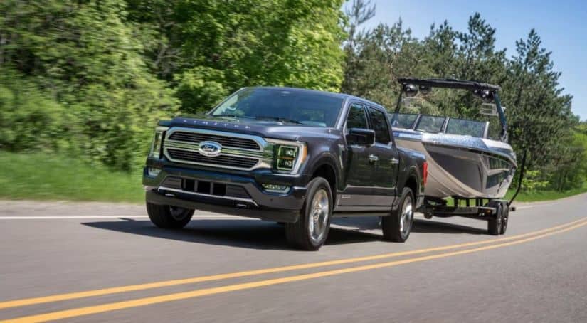 A black 2021 Ford F-150 Limited is towing a boat on a highway.
