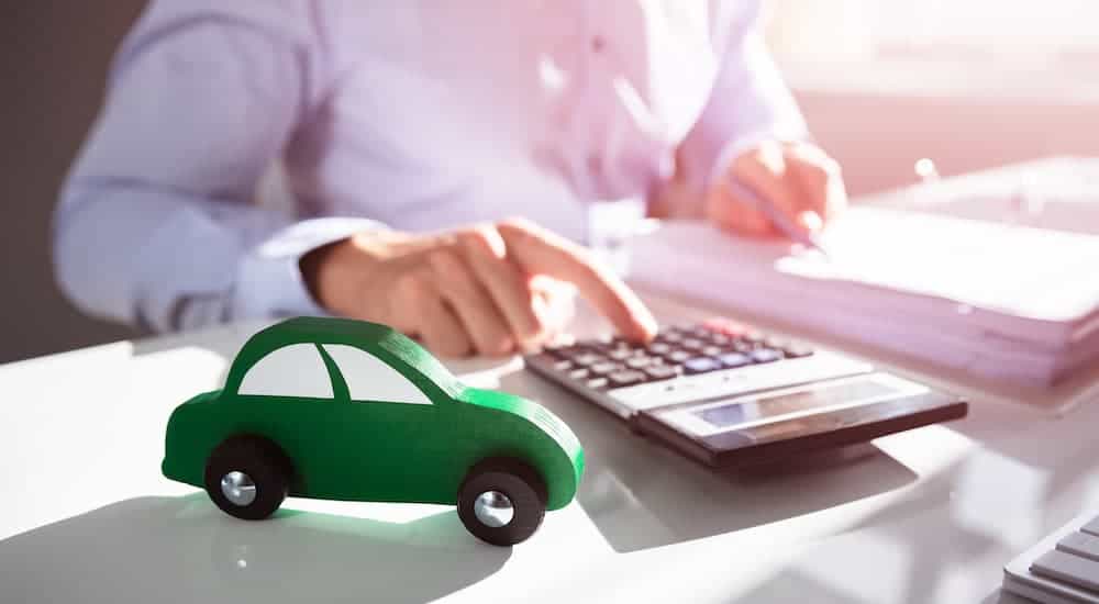A sales person is using a calculator with a green toy car on a desk.