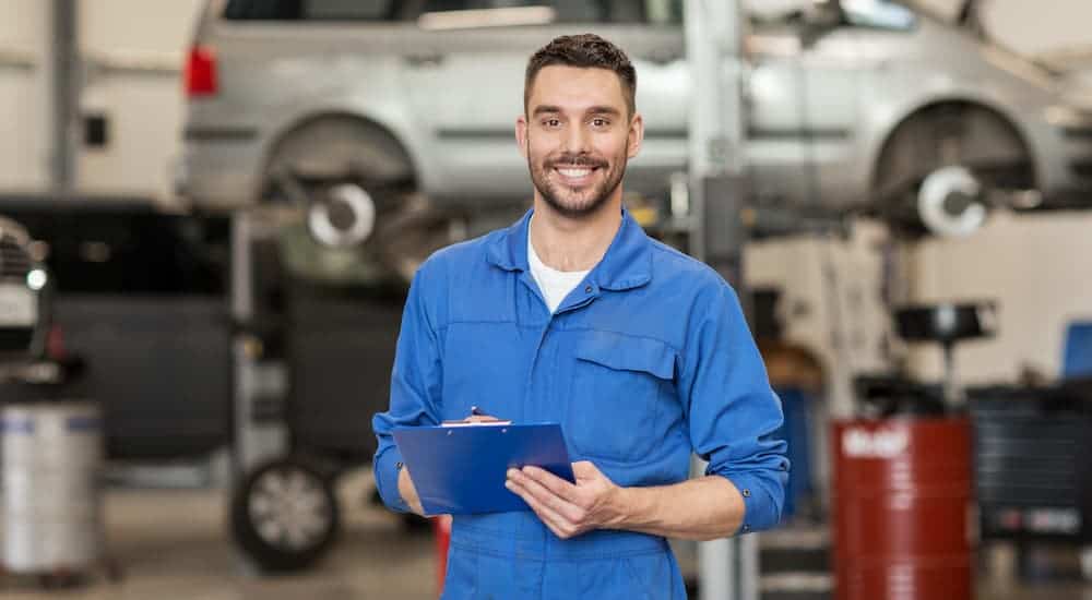 A service mechanic in a blue shirt is holding a clip board and smiling.