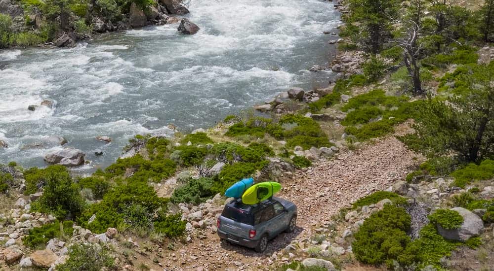 A blue 2021 Ford Bronco Sport 4-door is shown from a high angle next to a large river with kayaks on the roof.