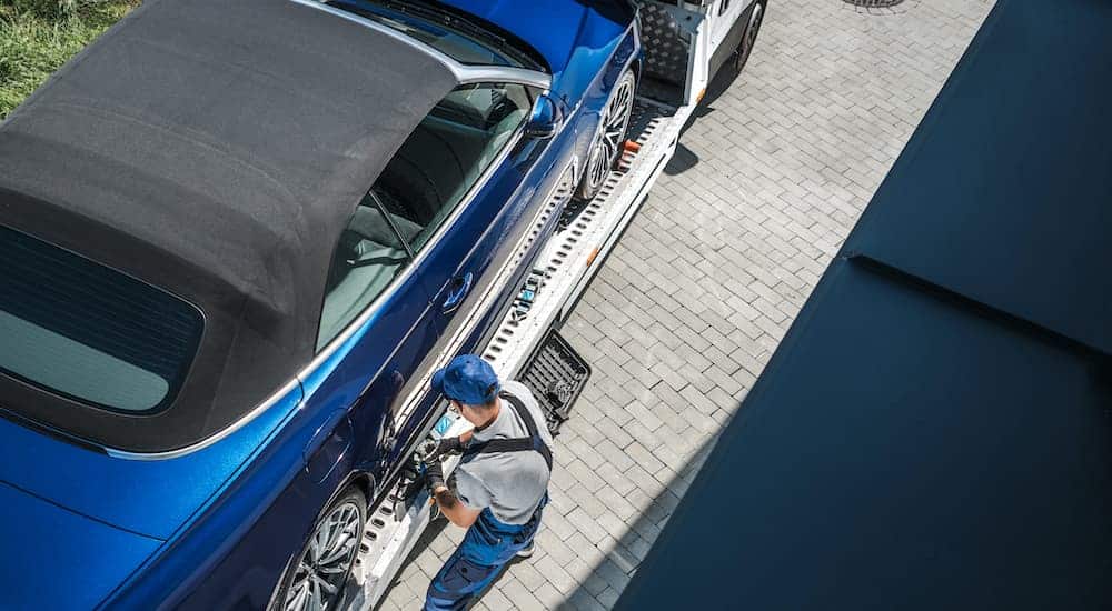A close up shows a tow truck driver removing the the tire straps on a blue convertible after being purchased on an online car sales site.