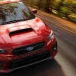 A red 2021 Subaru WRX is speeding down a wooded road after leaving a Subaru dealer in New Jersey.