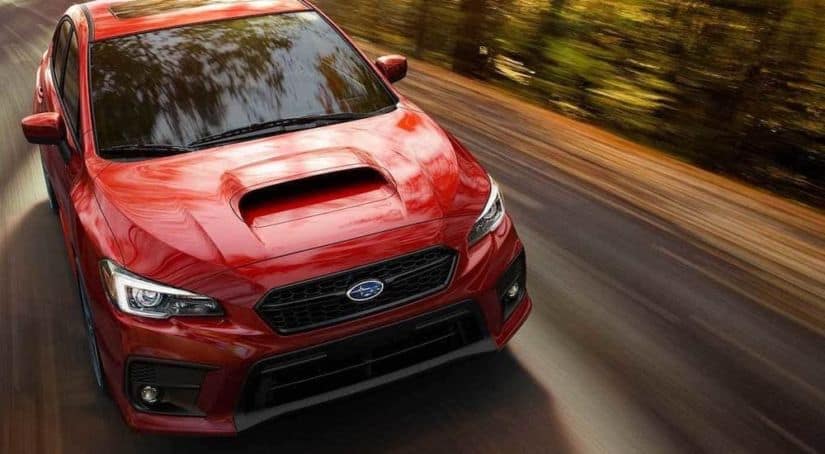 A red 2021 Subaru WRX is speeding down a wooded road after leaving a Subaru dealer in New Jersey.