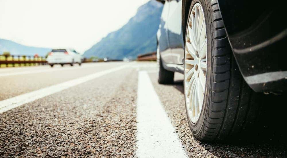 A closeup shows the white line on a highway next to the tire of a car.