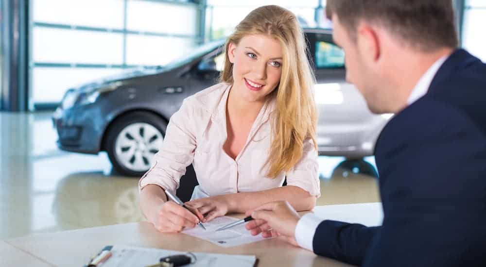 A young woman is signing paperwork at a used car dealer.