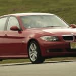A red 2005 BMW 325i is shown from the side driving past a field.