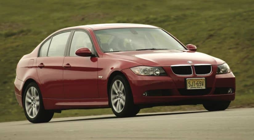 A red 2005 BMW 325i is shown from the side driving past a field.