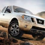A muddy white 2019 Nissan Frontier is driving on a dirt road.