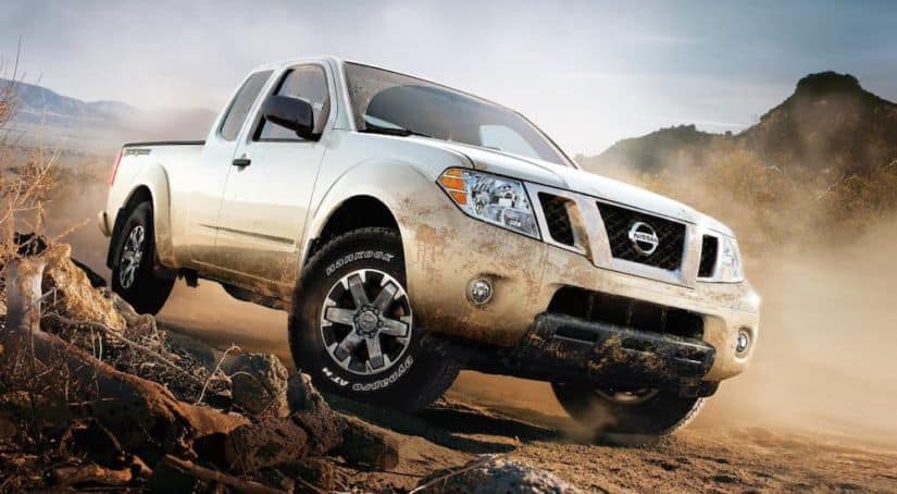 A muddy white 2019 Nissan Frontier is driving on a dirt road.