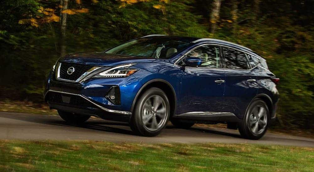 A blue 2019 Nissan Murano is driving in front of trees.