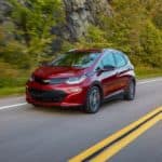 A red 2021 Chevy Bolt EV is driving on a rural highway.