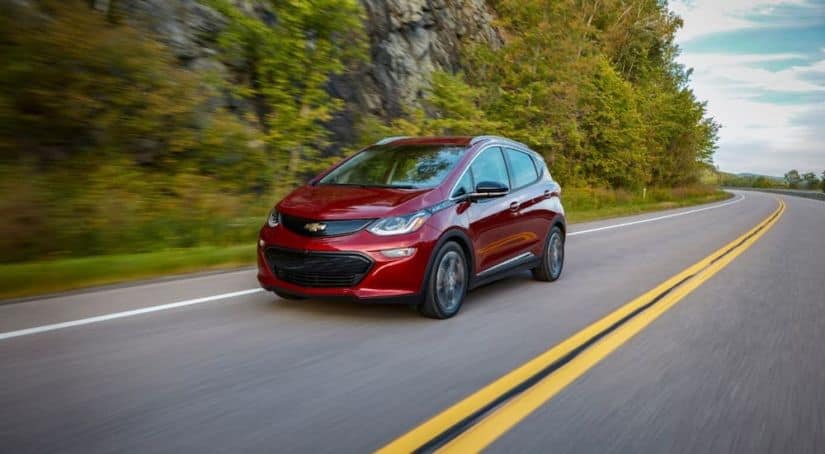 A red 2021 Chevy Bolt EV is driving on a rural highway.
