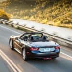A gray 2017 Fiat 124 Spider convertible is shown from the rear driving on a highway past a river after leaving a used Fiat dealer.