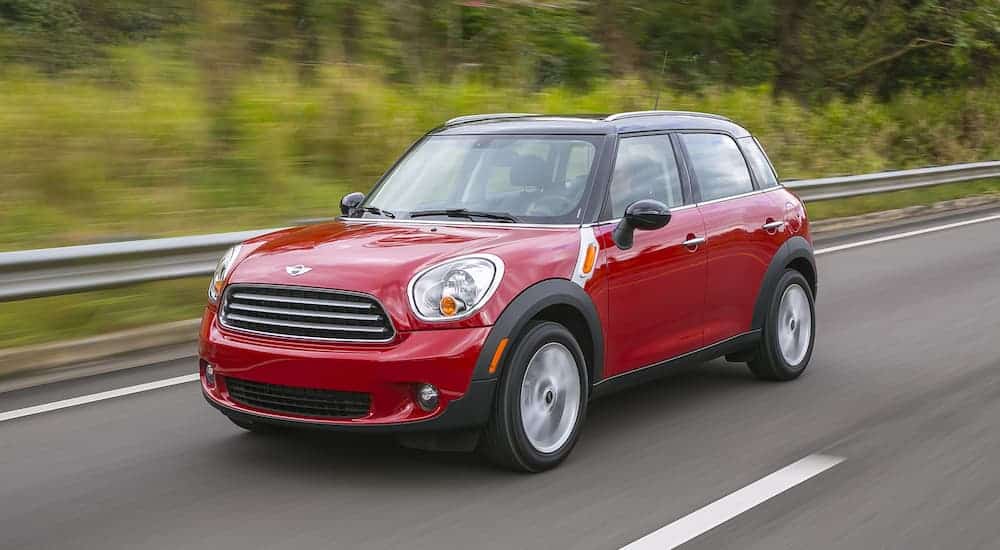 A red 2014 Mini Cooper Countryman, a popular used SUV for sale, is driving on a tree-lined road.