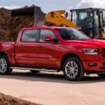 A man is directing a loader to put mulch in the bed of a red 2021 Ram 1500.