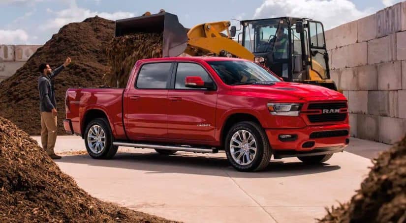 A man is directing a loader to put mulch in the bed of a red 2021 Ram 1500.