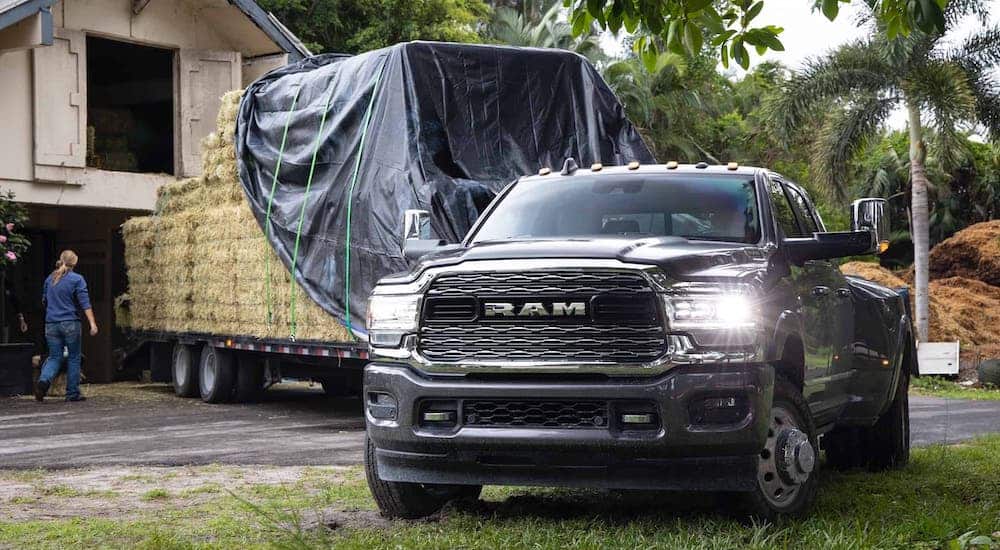A black 2021 Ram 3500 has a trailer full of hay in front of a barn.