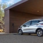 A silver 2021 Chevy Bolt EV is shown from behind while charging at a modern house.