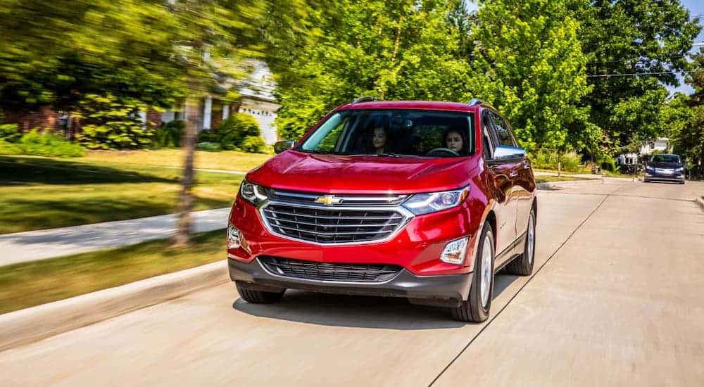 A red 2021 Chevy Equinox is driving on a suburban road.