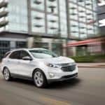 A white 2021 Chevy Equinox is driving in a city as part of the 2021 Chevy Equinox vs 2021 Kia Sportage comparison.