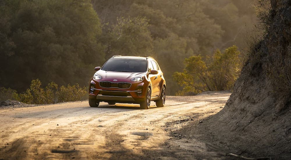 A red 2021 Kia Sportage is driving on a dirt road.