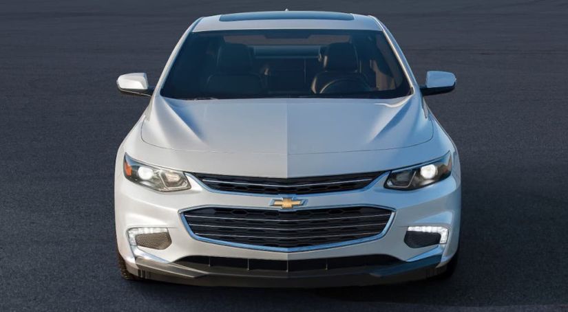 A white 2021 Chevy Malibu is shown from the front in an empty lot.