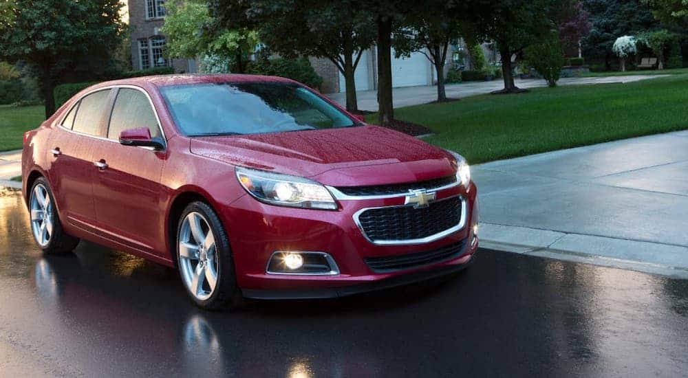 A red 2021 Chevy Malibu is driving on a wet road.