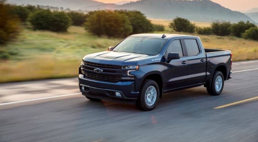 A blue 2021 Chevy Silverado 1500 RST is driving on a rural road after winning the 2021 Chevy Silverado 1500 vs 2021 GMC Sierra 1500 comparison.