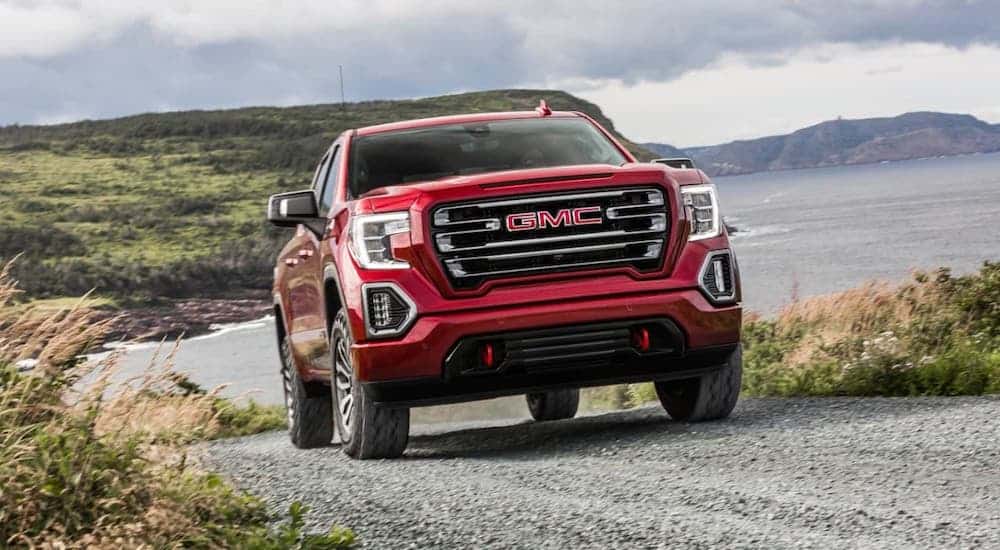 A red 2021 GMC Sierra 1500 is driving on a coastal dirt road.